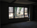 Wood paneled family room. Masonry fireplace with floor hearth, side built in shelving, netural carpet, and mega window wall to view wooded exterior. A mix of pines and hardwoods surround backyard patio